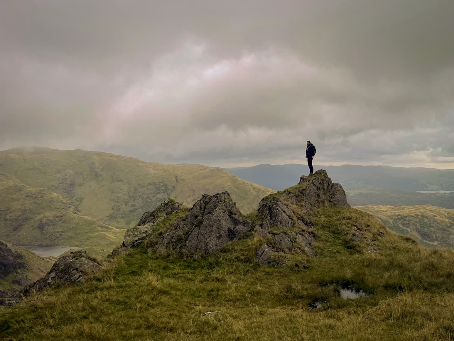 A person standing on a rocky mountain ridge overlooking hills